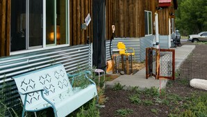 A wooden building with a large window, a bench, and a small table with chairs outside.