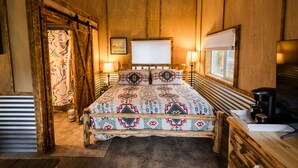 A rustic wooden room with a bed, bedside lamps, a window, and a mounted television.