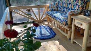 A wooden deck with a sofa and a table, a potted plant, and a view of a forest through a large window.