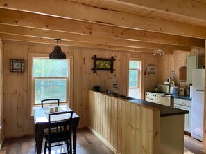 A wooden cabin interior with a kitchen area, dining table, and chairs. - Secluded River Overlook Cabin  on 160 acres (Potsdam)