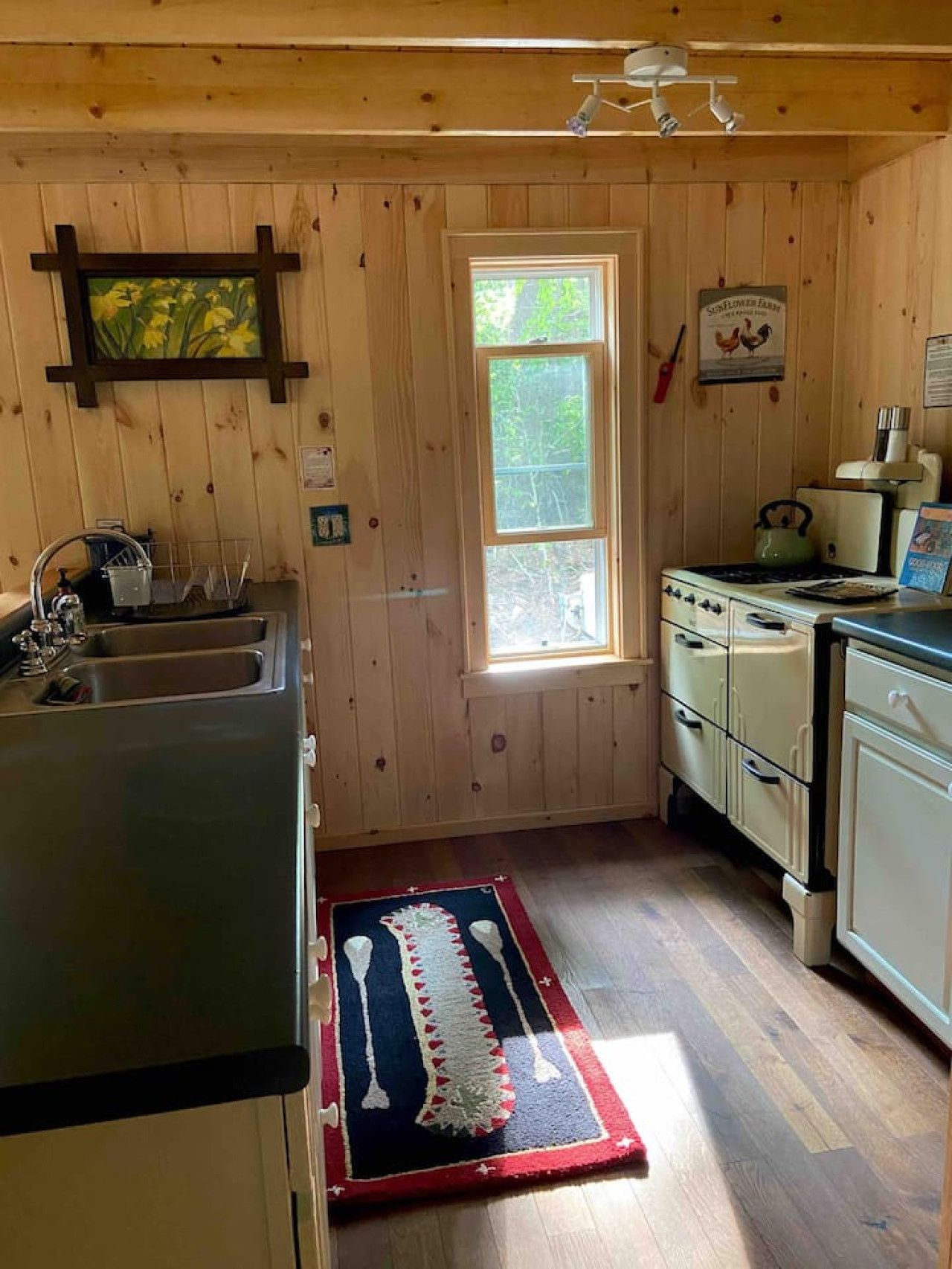 A kitchen with wooden walls, a window, a sink, a stove, and cabinets.