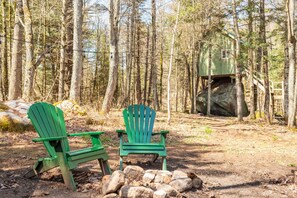 Two green Adirondack chairs in a forested area with a small cabin in the background. - The Rock House up in the trees! (Potsdam)