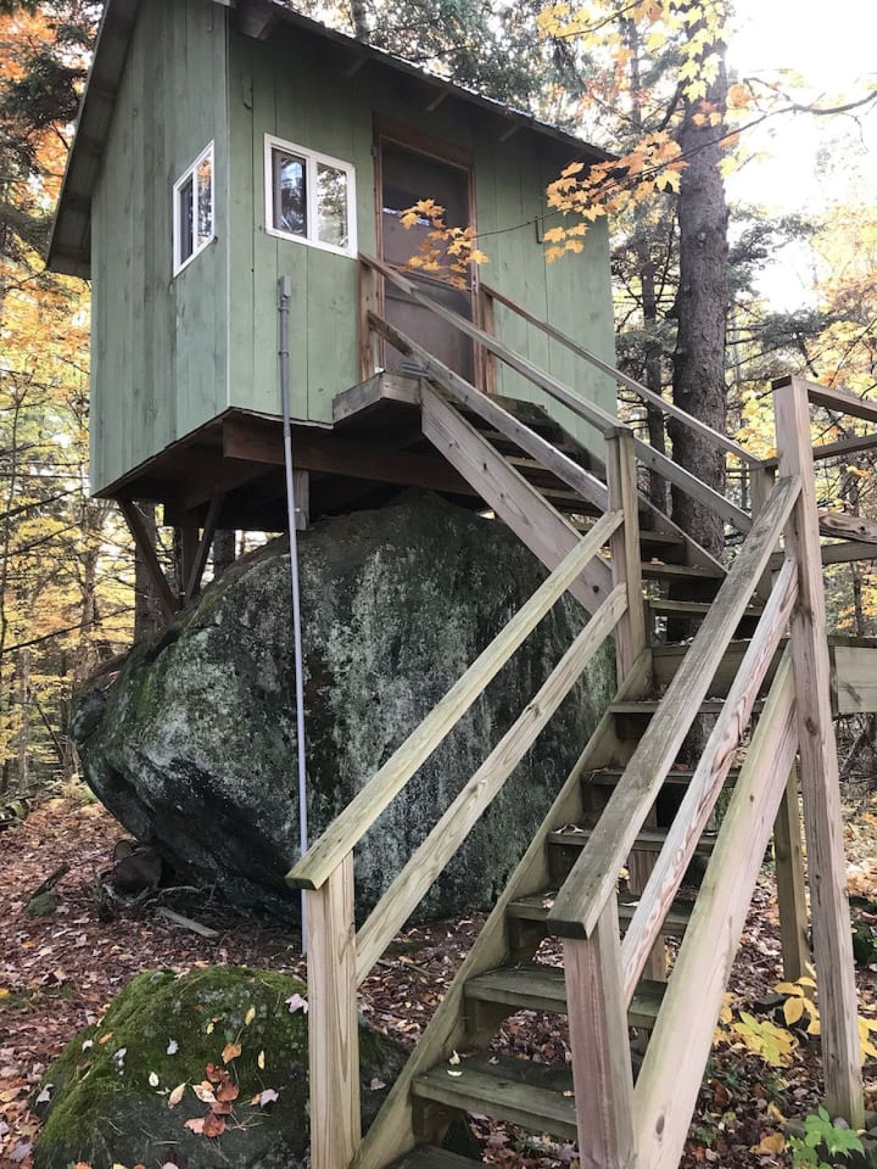 A treehouse with a wooden staircase and a small door, built on a large rock.
