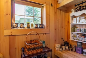 A wooden cabin interior with a window, shelves with jars, and a woven basket on a table. - The Rock House up in the trees! (Potsdam)
