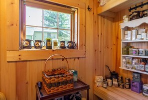 A wooden cabin interior with a window, shelves with jars, and a woven basket on a table.