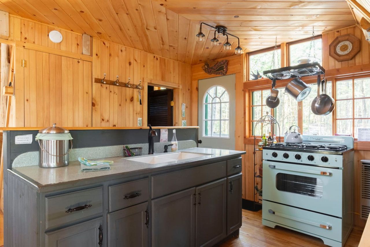 Una cocina con paredes de madera, un lavamanos grande, una estufa y ollas colgantes.