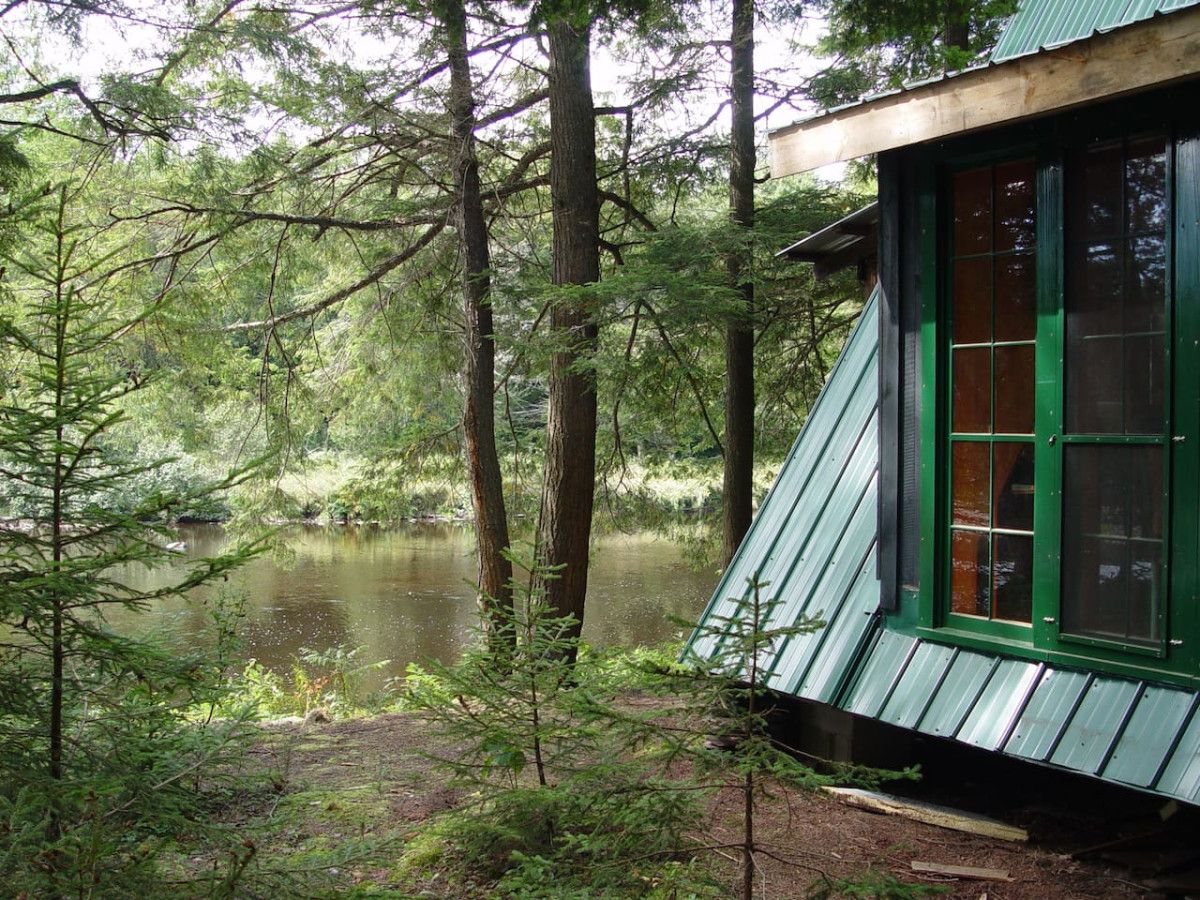 A cabin with a green roof and windows, surrounded by a forest and a lake.