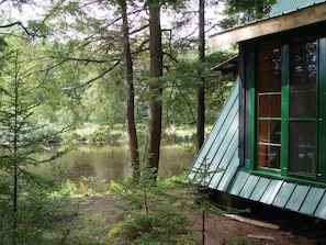 A cabin with a green roof and windows, surrounded by a forest and a lake. - Riverside Cabin & Nature Trails (Potsdam)