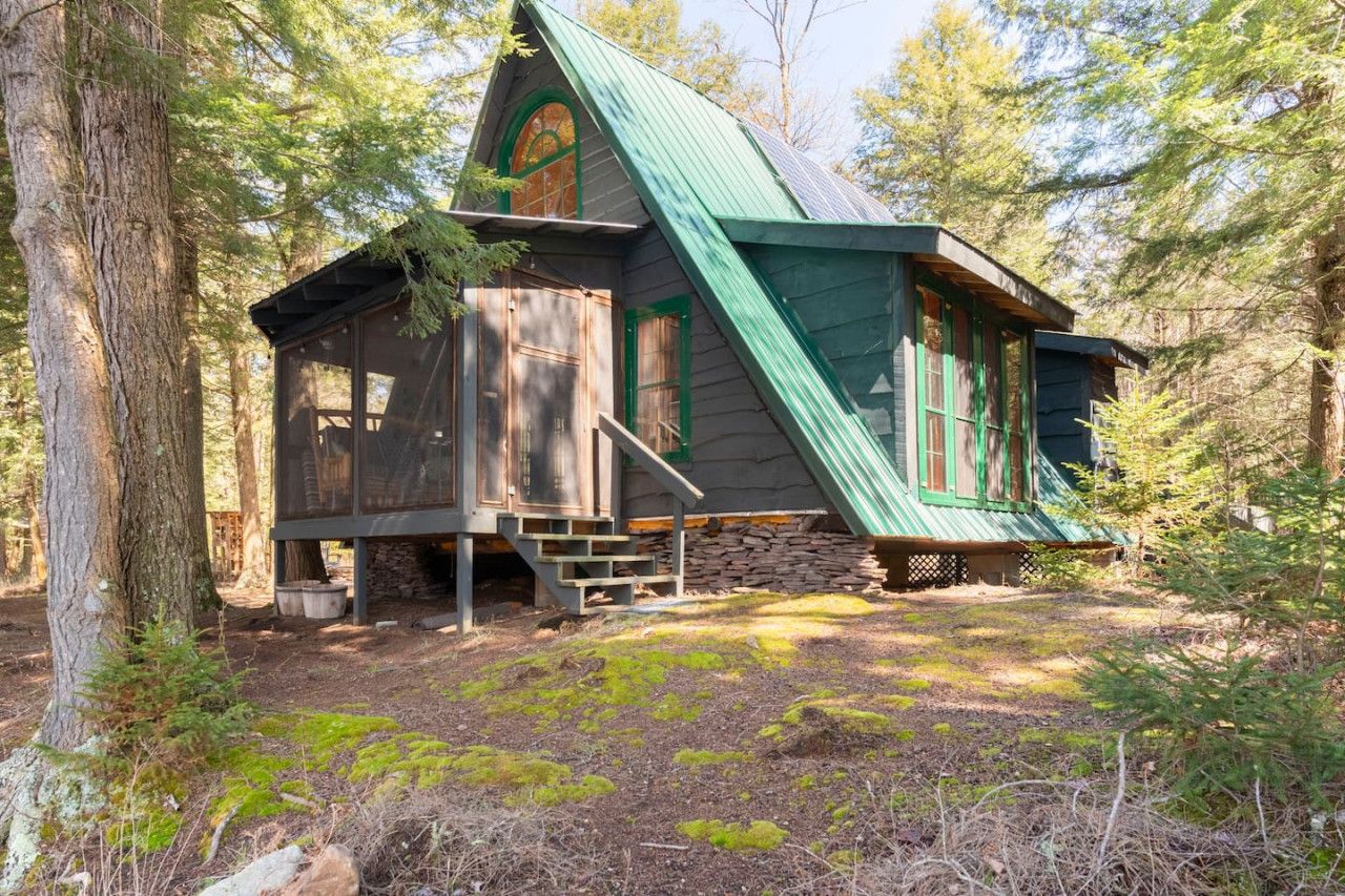 A rustic cabin with a steeply pitched roof, wooden exterior, and a stone foundation.