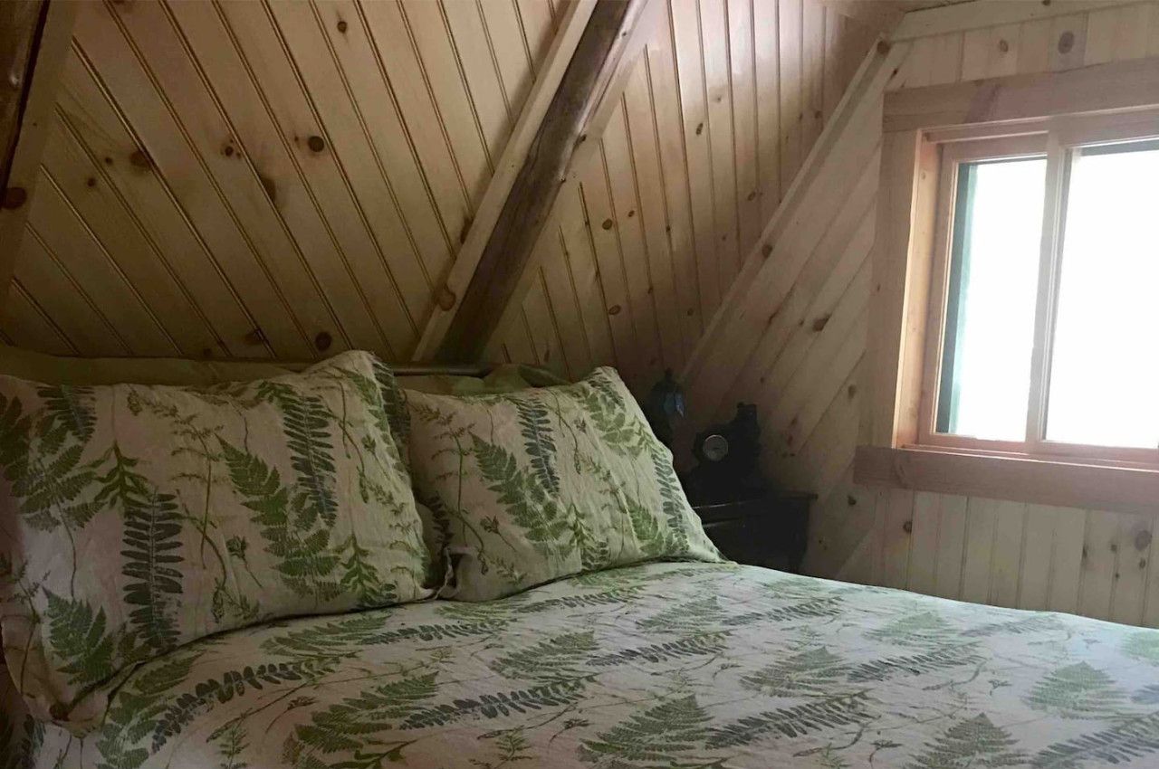 A bedroom with a sloped ceiling, a bed with a leaf-patterned bedspread, and a window with a view of the outdoors.