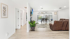 Ein modernes Wohnzimmer mit einem braunen Ledersofa, einer Topfpflanze und einem Essbereich mit einer Glastür, die nach draußen führt.