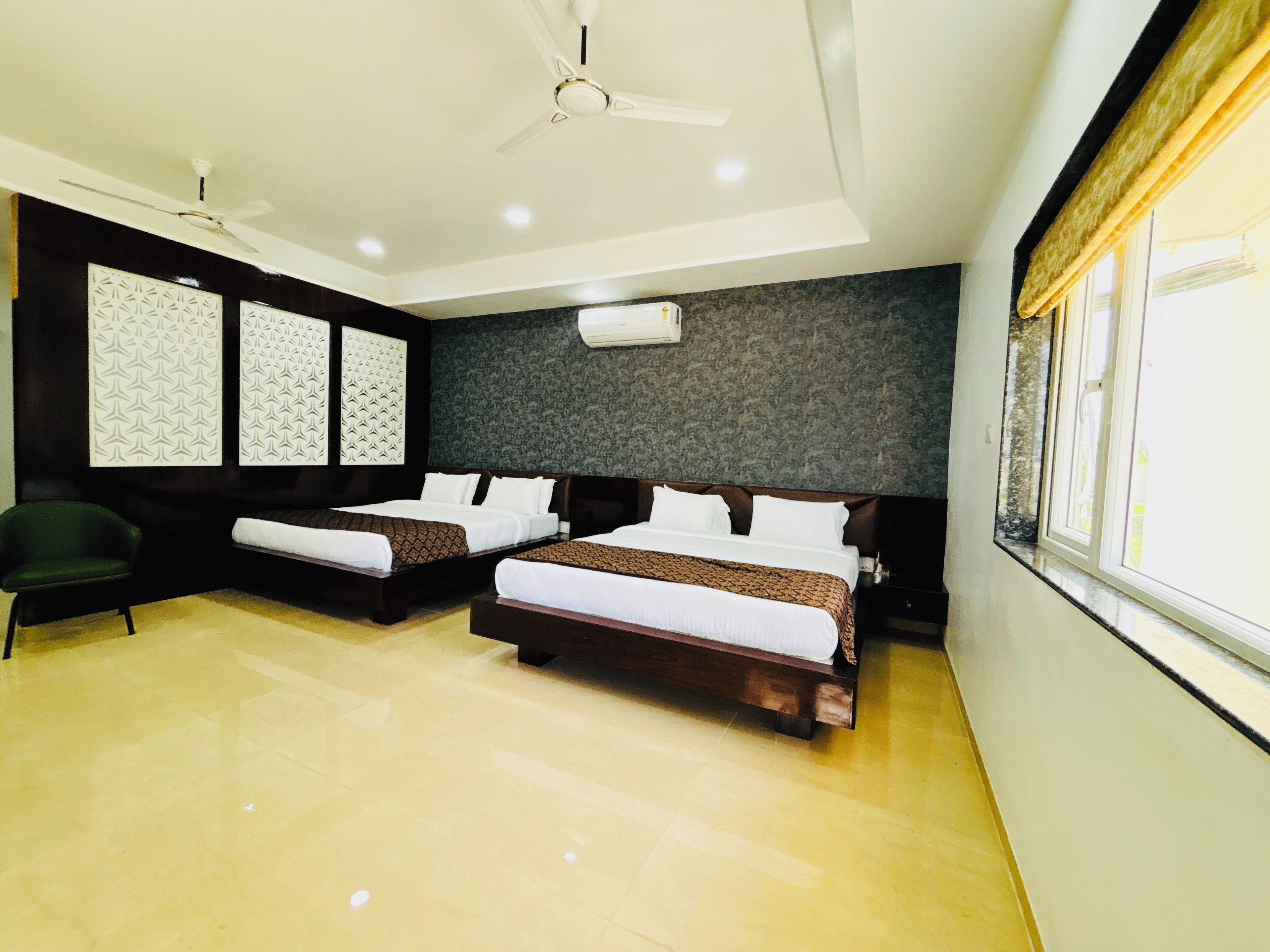 A hotel room with two beds, a ceiling fan, a green chair, and a window with curtains.