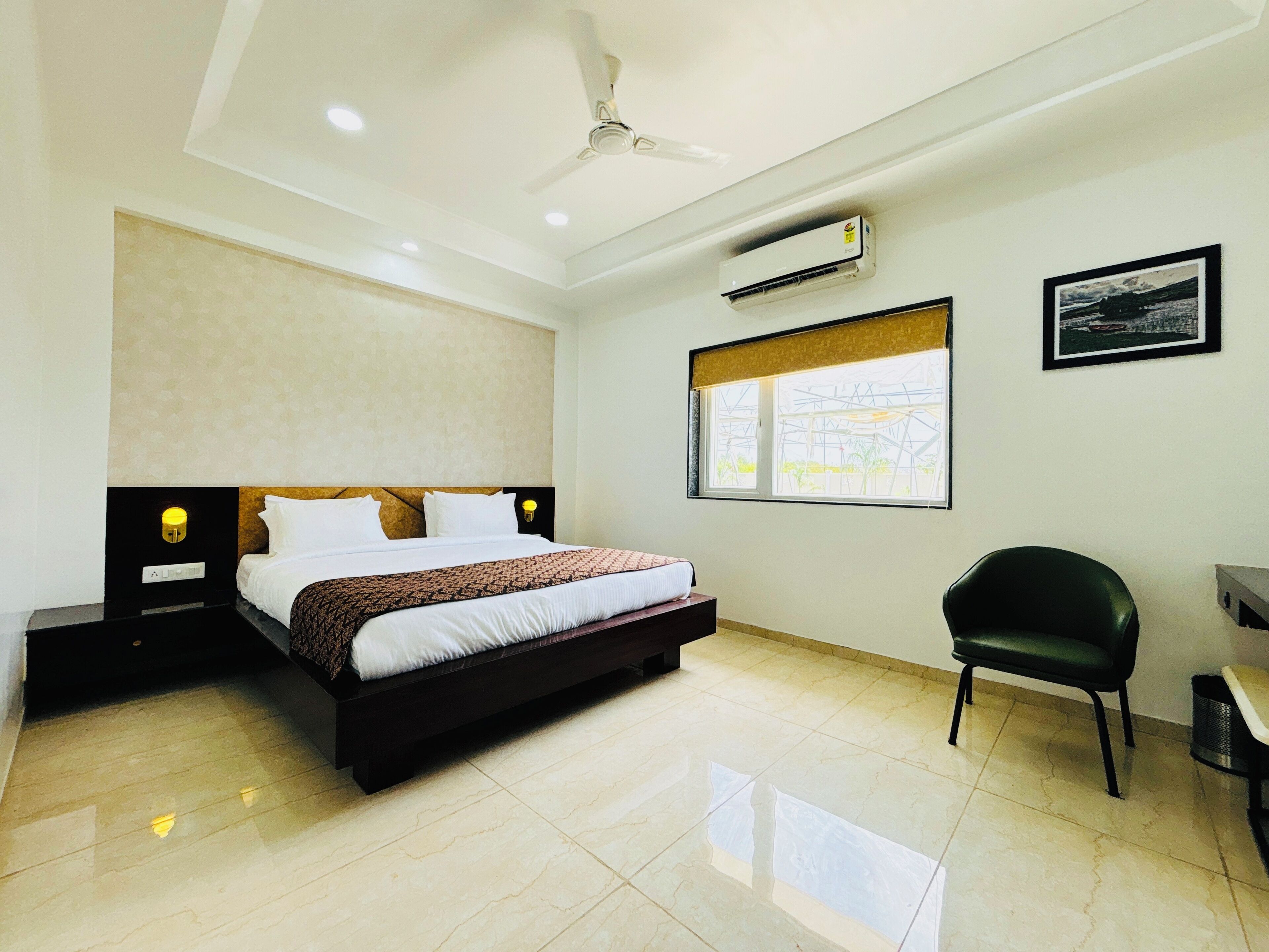 A modern hotel room with a large bed, a desk, a chair, an air conditioning unit, and a window with a view.