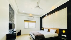 Un dormitorio moderno con cama, televisión, ventilador de techo y ventana.