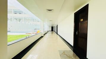 A long, well-lit corridor with a marble floor, a glass wall on one side, and a dark door on the other.