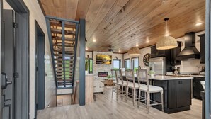 A modern kitchen with dark cabinetry, a central island, and a dining area with wicker chairs. - Luxury Escape: Private Pool, Theatre & Waterpark • 6mi Dollywood • 1mi Parkway (Sevierville)
