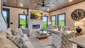A modern living room with a stone fireplace, comfortable seating, and a large wall clock. - Luxury Escape: Private Pool, Theatre & Waterpark • 6mi Dollywood • 1mi Parkway (Sevierville)