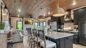 A modern kitchen with dark cabinetry, a central island, and a dining area with a sofa and chairs. - Luxury Escape: Private Pool, Theatre & Waterpark • 6mi Dollywood • 1mi Parkway (Sevierville)