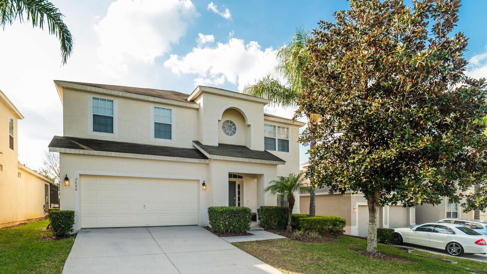 A two-story house with a garage, a small front yard, and a tree.