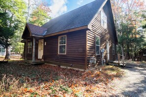 A rustic wooden cabin with a steeply pitched roof, a front porch, and a small staircase leading to the entrance.