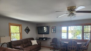 A living room with a brown leather couch, a television, and a ceiling fan. - Cabin with private peninsula on Presque Isle Chain of Lakes! (Presque Isle)