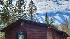 A small, rustic cabin with a steeply pitched roof, a chimney, and a small porch with a staircase. - Cabin with private peninsula on Presque Isle Chain of Lakes! (Presque Isle)