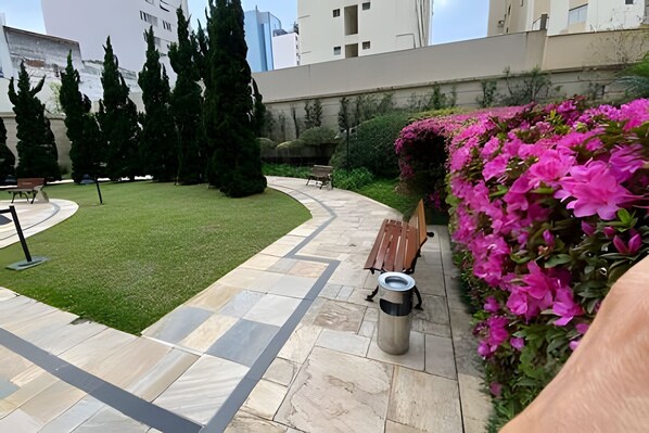 A courtyard with a curved pathway, benches, and a trash can. - Studio Living Mercure Pinheiros (São Paulo)