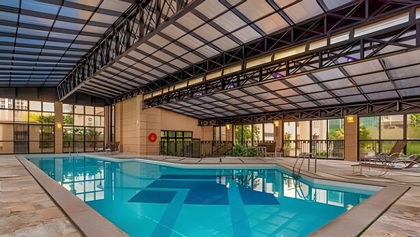 A large indoor swimming pool with a covered roof, stone flooring, and lounge chairs along the poolside. - Studio Living Mercure Pinheiros (São Paulo)