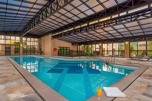 A large indoor swimming pool with a covered roof, stone flooring, and lounge chairs along the poolside. - Studio Living Mercure Pinheiros (São Paulo)