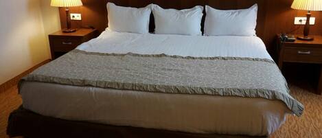 A neatly made bed with a patterned bedspread and pillows, flanked by two bedside tables with lamps.