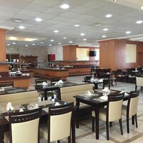 Un restaurante espacioso con varias mesas y sillas, una zona de barra y un televisor montado en la pared.