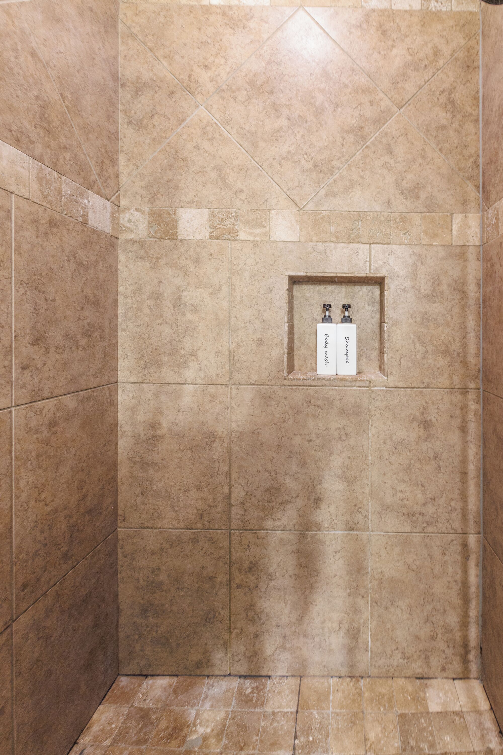 A tiled shower area with a small shelf containing two bottles labeled "Shampoo" and "Body Wash".