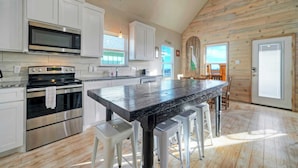 A modern kitchen with white cabinets, stainless steel appliances, and a wooden floor. - 2 Homes, Sleeps 16, Shared Pool+boat Dock Laguna Village Serenity by Avantstay (Corpus Christi)