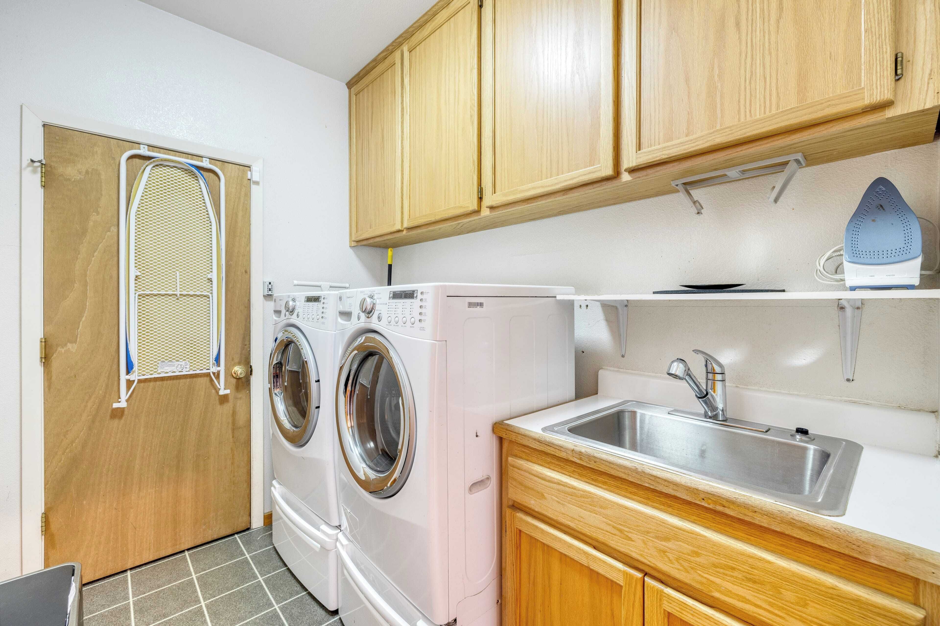 A laundry room with two washing machines, a sink, wooden cabinets, and a drying rack.