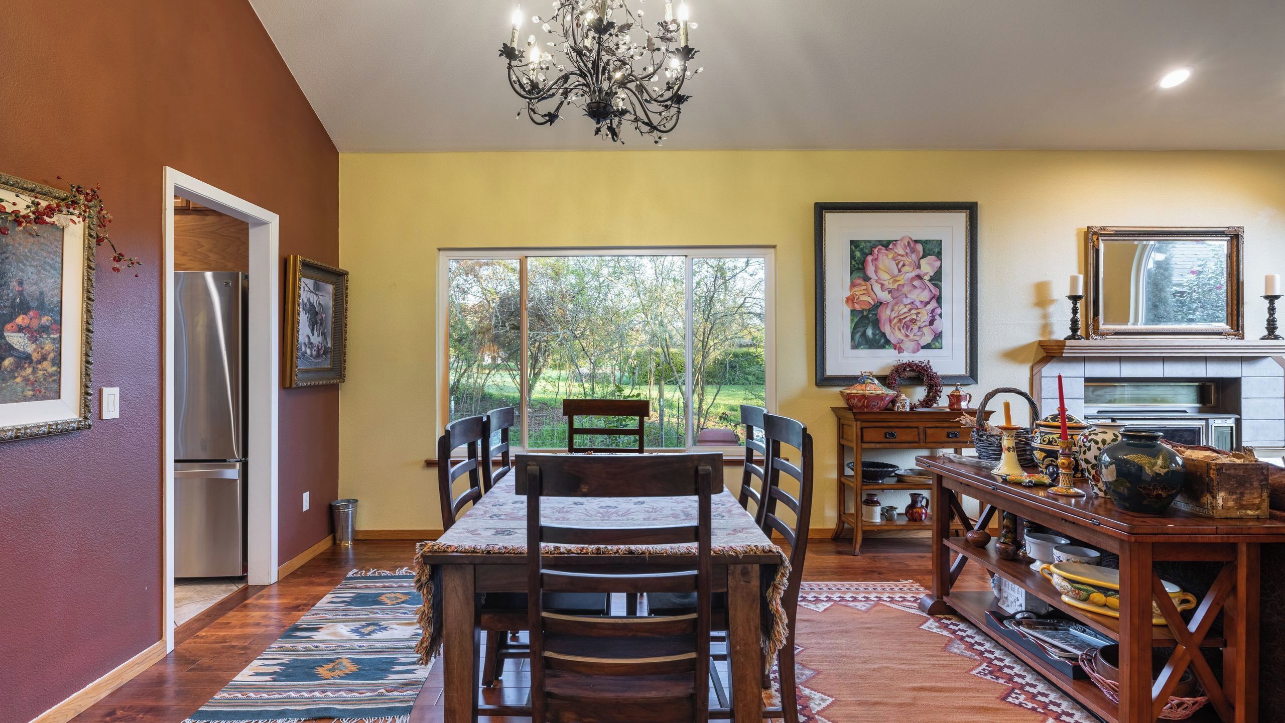A dining area with a table, chairs, a chandelier, and a view of the outdoors.