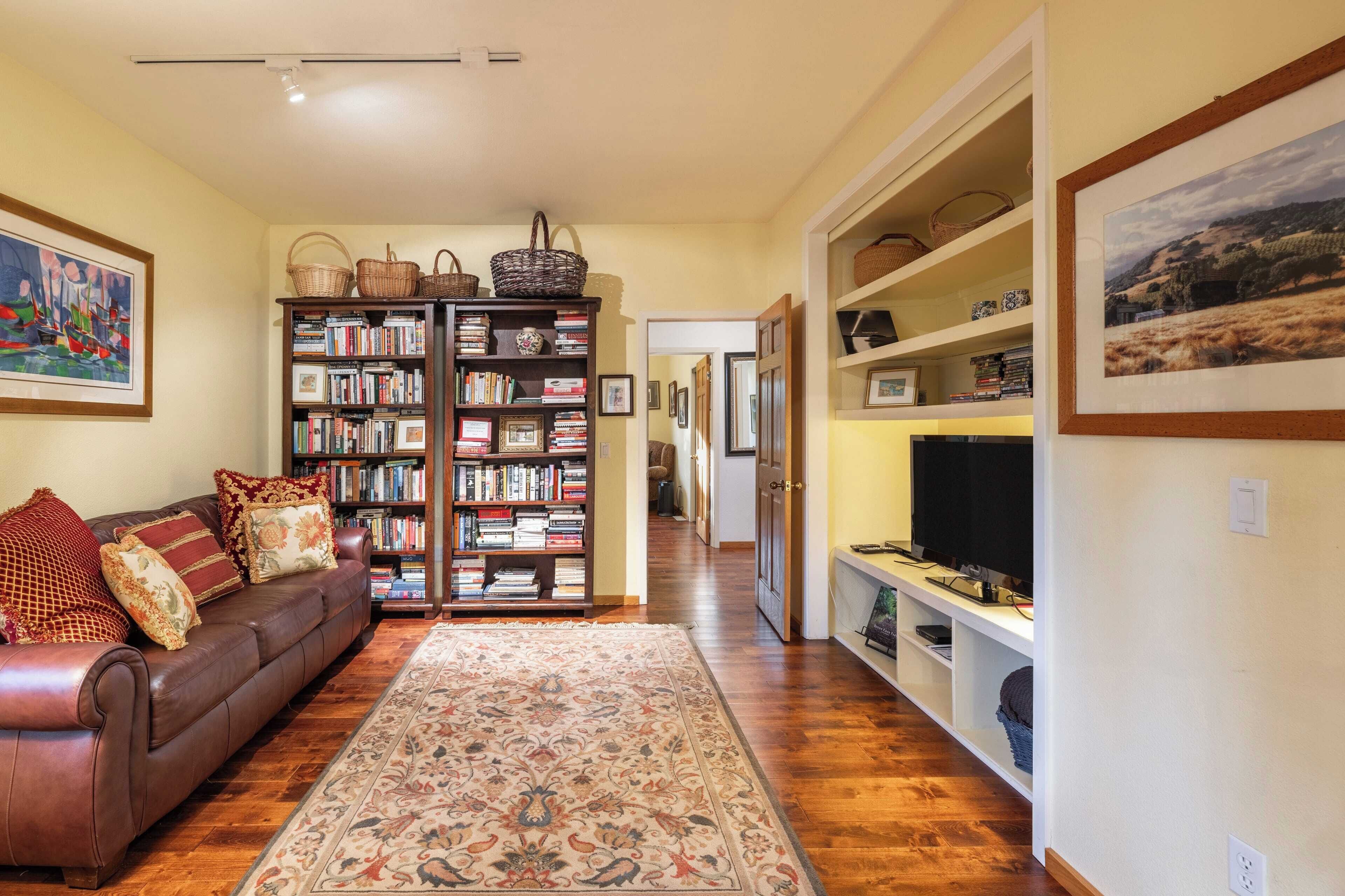 A living room with a brown leather sofa, a large bookshelf, and a television on a stand.