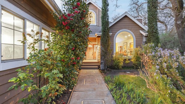 A house with a covered porch, a stone pathway, and a garden with various plants and flowers.