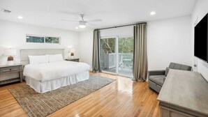 A bedroom with a bed, nightstands, a desk, a chair, a ceiling fan, and a balcony with curtains. - Dolphin Days by Avantstay Pool, 0.2mi to Beach! (Destin)