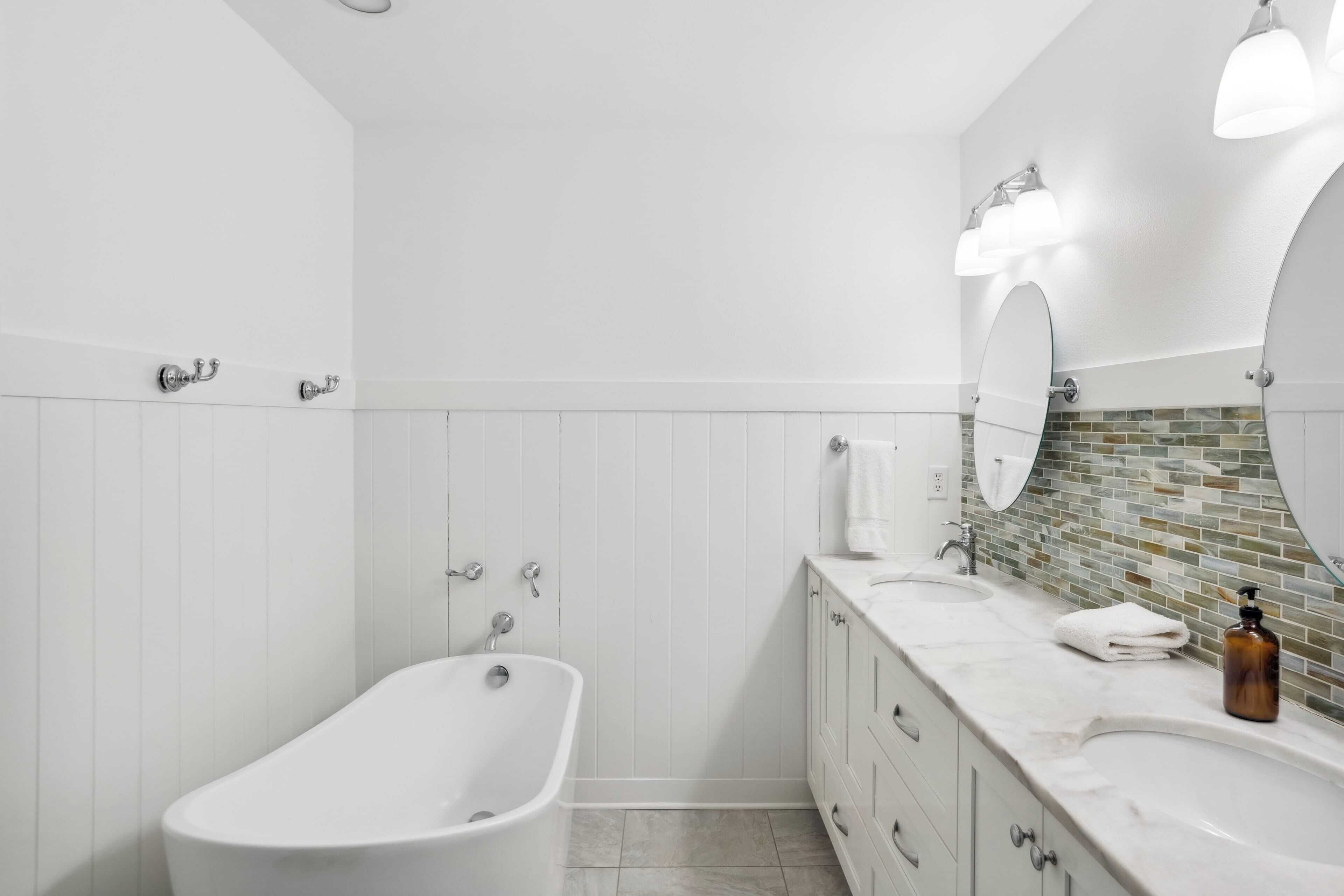 A modern bathroom with a freestanding bathtub, a vanity with a mirror, and a tiled backsplash.