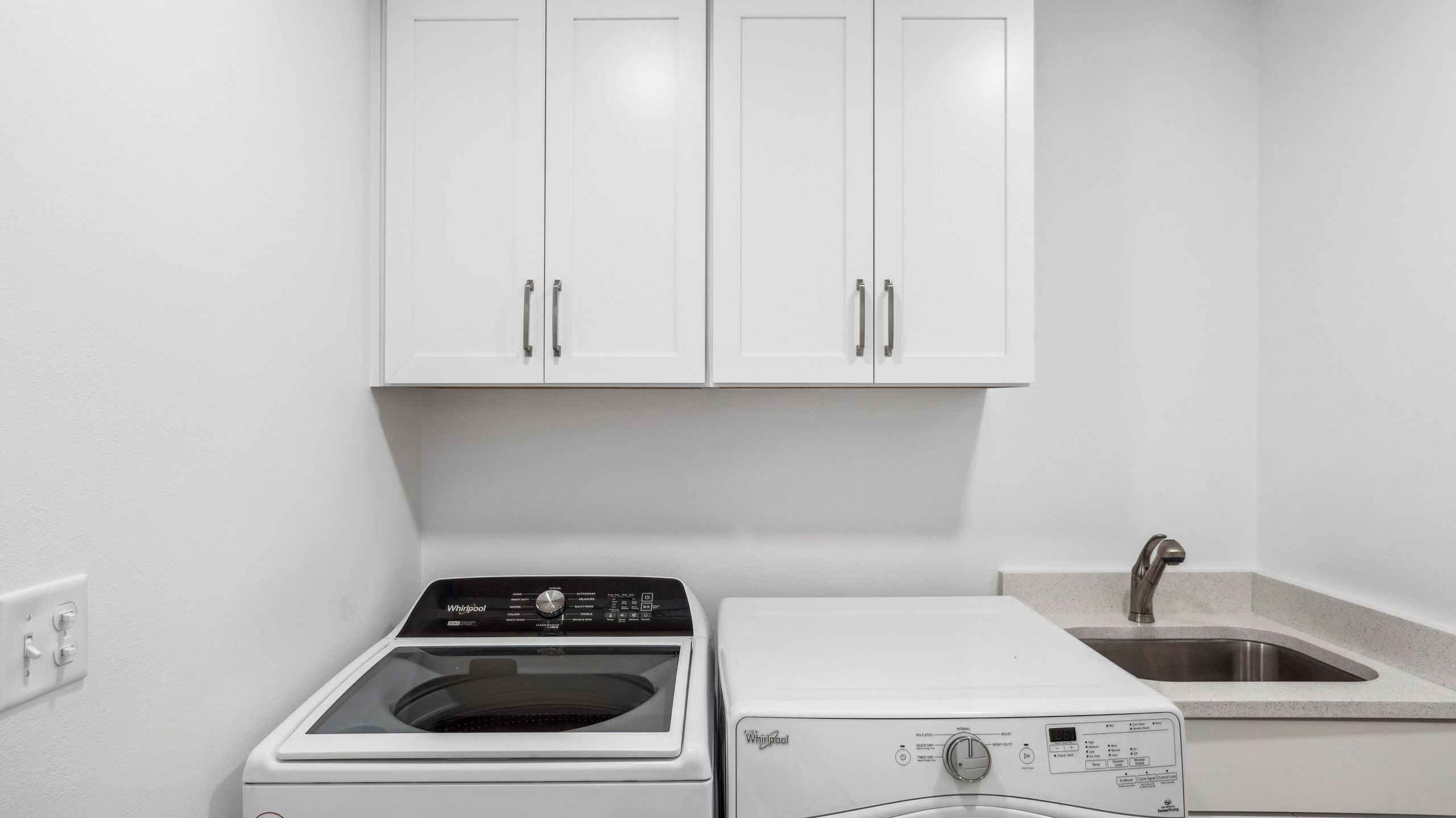 A laundry room with a washer and dryer, a sink, and white cabinets.