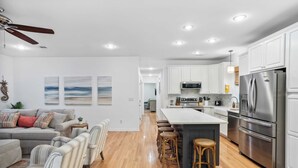 A modern kitchen with white cabinets, stainless steel appliances, and a central island with stools. - Dolphin Days by Avantstay Pool, 0.2mi to Beach! (Destin)