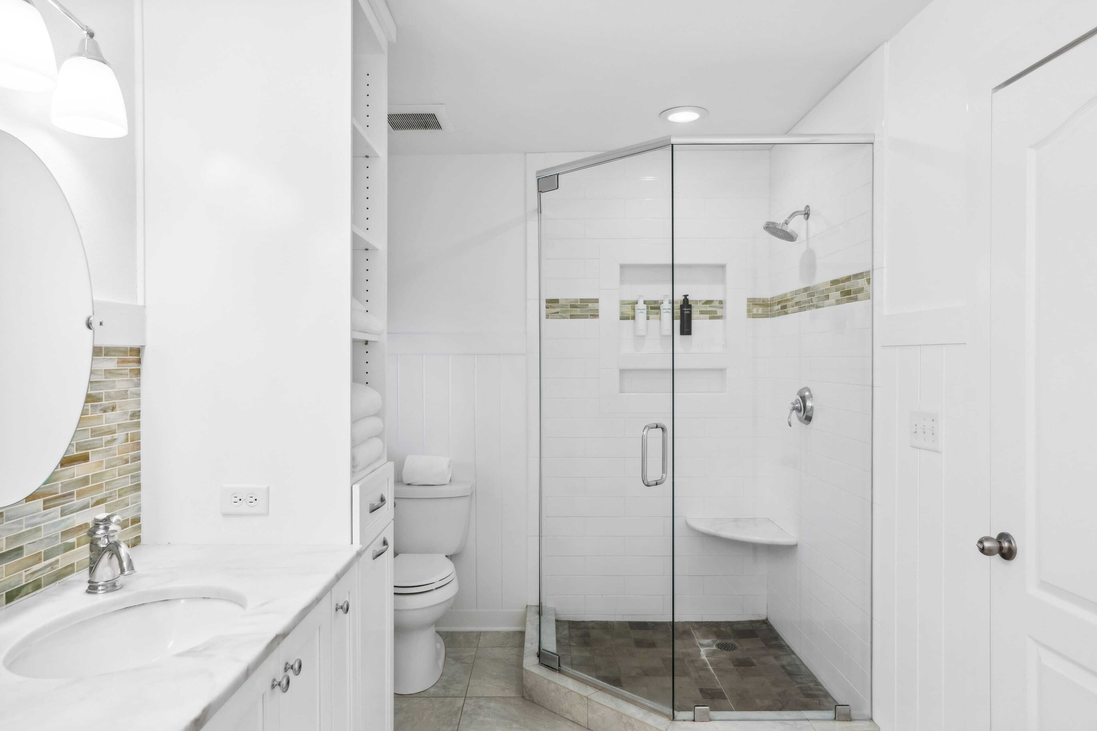 Un baño moderno con ducha de vidrio, lavamanos blanco y retrete.