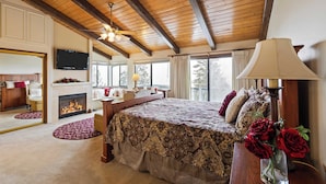 A spacious bedroom with a large bed, a fireplace, a television, and a view of the outdoors. - 6bdr Group Retreat, Decks w/ Incredible Views Starry Heights by Avantstay (Lake Arrowhead)