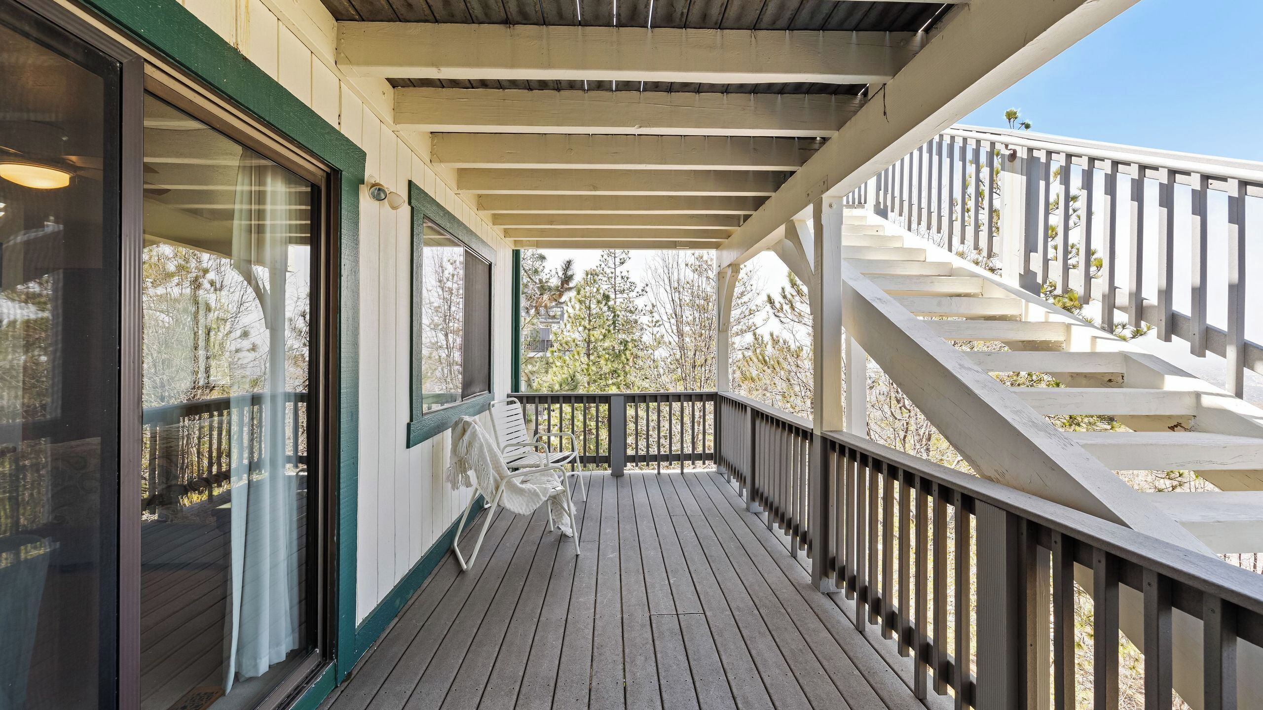 A wooden deck with a railing, a staircase, and a view of trees.