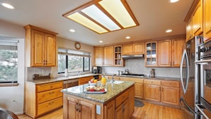 A spacious kitchen with wooden cabinets, a granite countertop, stainless steel appliances, and a large island with breakfast items. - 6bdr Group Retreat, Decks w/ Incredible Views Starry Heights by Avantstay (Lake Arrowhead)