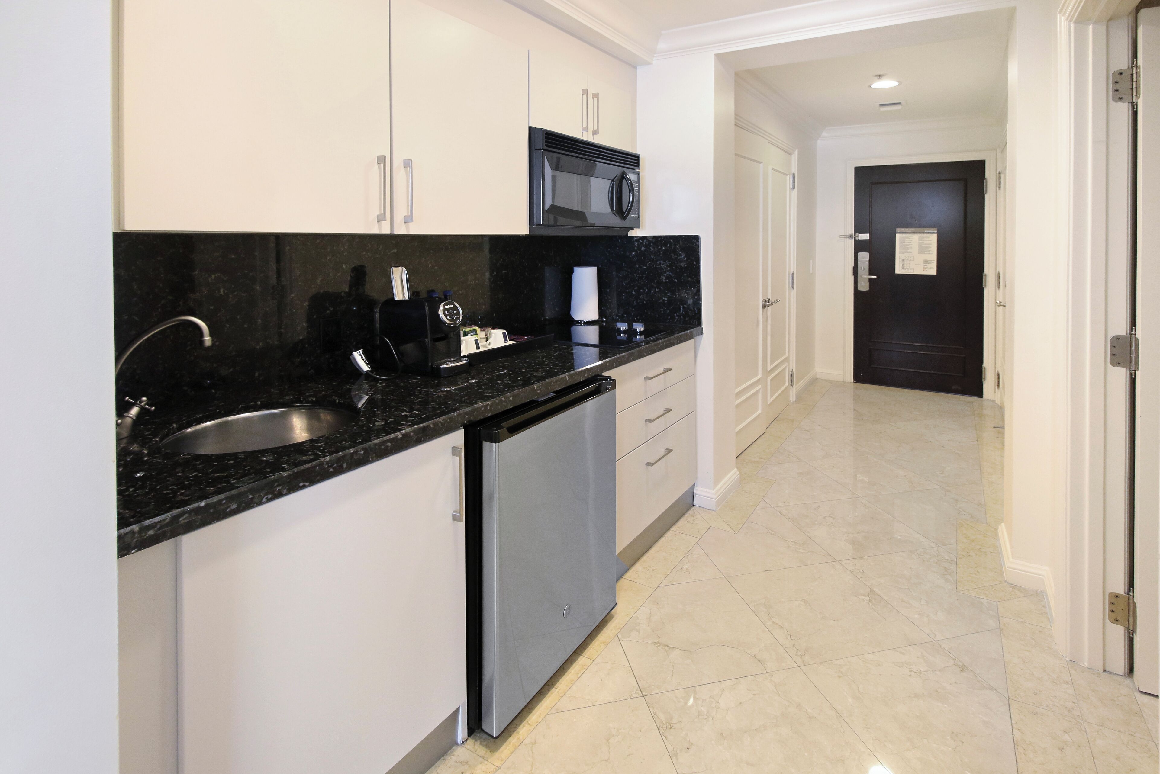 A modern kitchen with white cabinets, a black countertop, a built-in microwave, and a dishwasher.