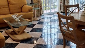 A living room with a checkered floor, a sofa, a glass coffee table, a chandelier, and a dining table with chairs.