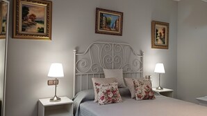 A neatly arranged bedroom with a bed, two bedside tables with lamps, and three framed paintings on the wall.