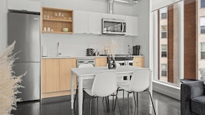 A modern kitchen with white cabinetry, a stainless steel refrigerator, and a dining area with a white table and chairs. - Cosmopolitan Calgary, Modern Loft (Calgary)