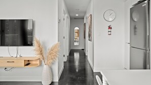 A modern hallway with a flat-screen TV, a wooden console, pampas grass, a fire extinguisher, and a refrigerator. - Cosmopolitan Calgary, Modern Loft (Calgary)
